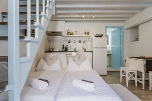 A bedroom with two beds, a kitchenette, and a bathroom visible through an open door.