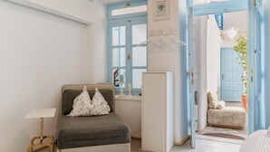 A room with a bed, a small table, a white cabinet, and a door leading to another room.