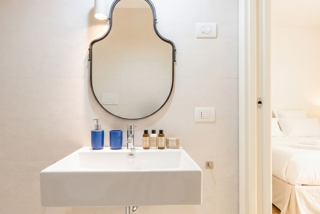 A bathroom with a white sink, a mirror with a black frame, a blue cup, and several toiletries.