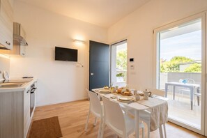 A modern kitchen with a dining area, a TV mounted on the wall, and a sliding glass door leading to an outdoor seating area.