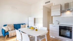 A modern kitchen with white cabinetry, a built-in oven, and a dining area with a white table and chairs. - Maison Aurora+ Pivate Parking Space (Bari)