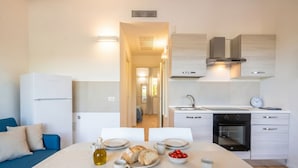 A compact kitchen with a dining area, white cabinetry, a built-in oven, and a visible clock. - Maison Aurora+ Pivate Parking Space (Bari)