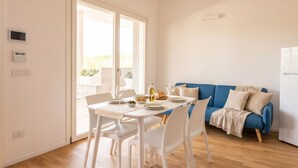 A modern living room with a dining table set for two, a blue sofa, and a sliding glass door leading to an outdoor area. - Maison Aurora+ Pivate Parking Space (Bari)