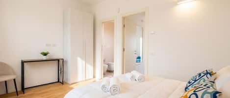 A bedroom with a bed, a desk, and a chair. There is a bathroom visible through an open door.