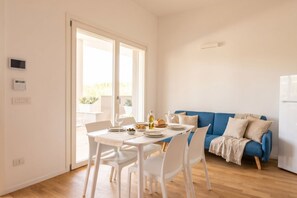Een moderne woonkamer met een eettafel gedekt voor twee personen, een blauwe bank en een glazen schuifdeur naar een buitenruimte.