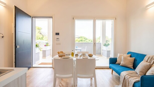 A modern interior with a dining area, a blue sofa, and a kitchen counter. - Maison Aurora+ Pivate Parking Space (Bari)