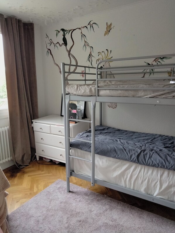 A bunk bed with a ladder, a white dresser, and a radiator.