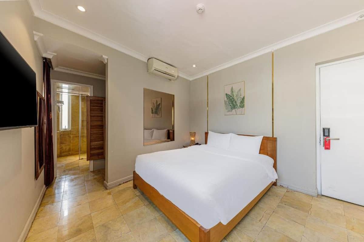 Une chambre d’hôtel avec un grand lit, un téléviseur à écran plat, un appareil de climatisation, une porte avec une poignée rouge et un tableau encadré au mur.