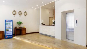 Ein Hotel-Empfangsbereich mit einem Pepsi-Automaten, einer Rezeption, einem Spiegel und einem Aufzug.
