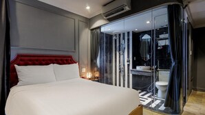Ein Hotelzimmer mit einem großen Bett, einem durch eine Glaswand abgetrennten Badezimmer und einem modernen Design.