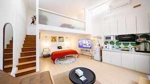 Un appartement moderne avec une chambre en mezzanine, une cuisine équipée d’un four à micro-ondes et d’une machine à café, ainsi qu’un petit coin repas.