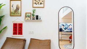 Un salon moderne avec un canapé, un grand miroir et des éléments de décoration murale, notamment un tableau représentant un cerf encadré, un motif en bois encadré et un panneau rouge portant un caractère chinois.