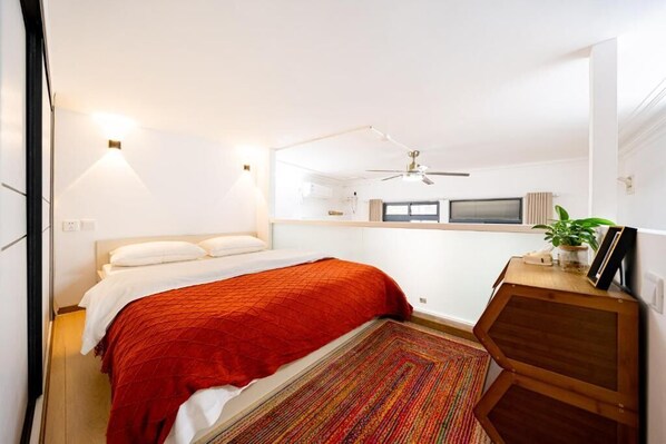 Een slaapkamer met een bed, een plafondventilator, een tafeltje met een plant en een raam.