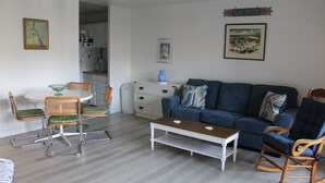 A living room with a blue sofa, wooden rocking chairs, a white coffee table, and a dining table with wicker chairs. - Studio & 1 Bath in Rehoboth Beach - Ocean Block (Rehoboth Beach)