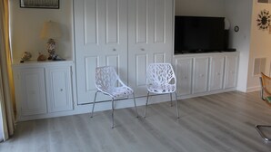 A room with a large white wardrobe, a flat-screen TV, two white chairs, and a small table with decorative items. - Studio & 1 Bath in Rehoboth Beach - Ocean Block (Rehoboth Beach)