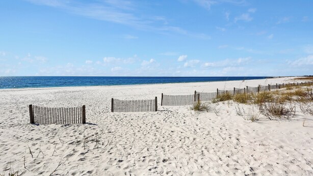 Ein sandiger Strand mit einer Holzlattenveranda und blauem, wolkenlosem Himmel.