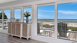 Una stanza con ampie finestre vista spiaggia, un armadio bianco con un vaso di fiori e un patio in legno all'esterno.