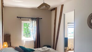 Un dormitorio con cama, ventana con cortinas, lámpara colgante y vistas al exterior.