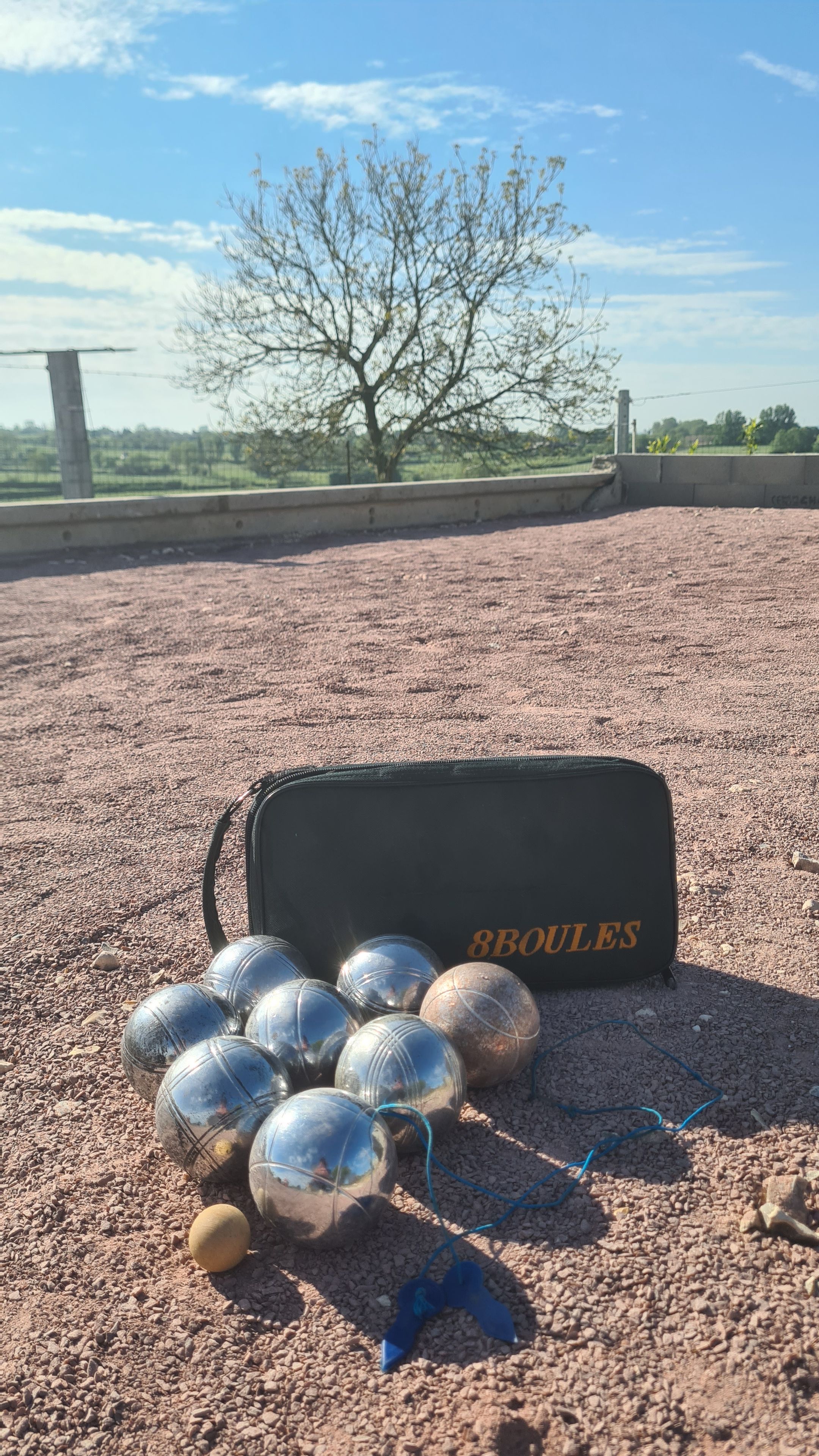 Un sac étiqueté « 8 BOULES » sur une surface de gravier, avec plusieurs balles et un objet bleu.