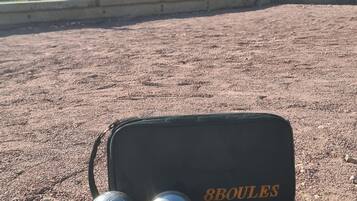 Un sac étiqueté « 8 BOULES » sur une surface de gravier, avec plusieurs balles et un objet bleu.