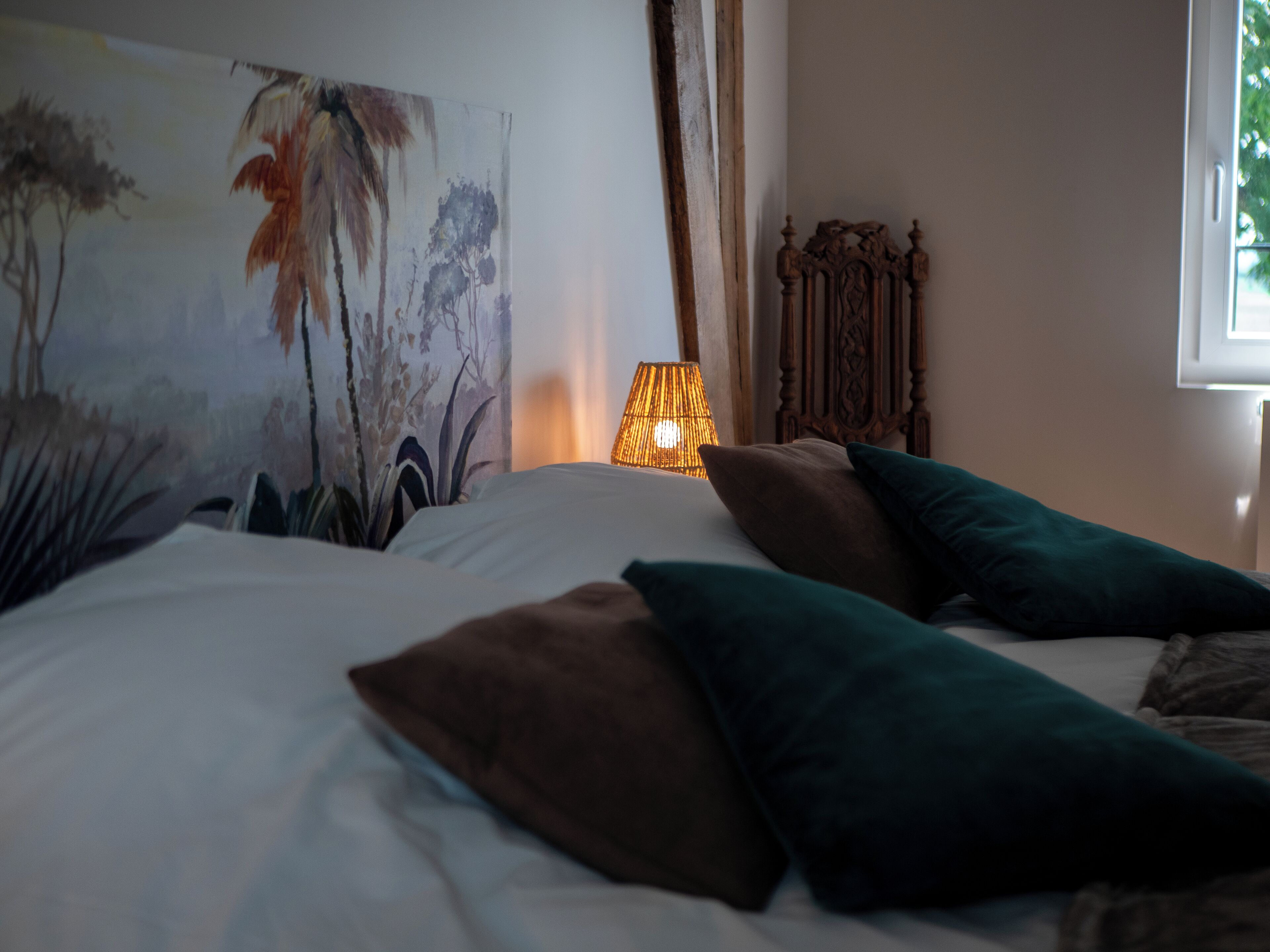 A bedroom with a bed, pillows, a lamp, and a painting on the wall.