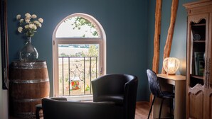 Una habitación con vistas a través de un amplio ventanal, un barril de madera, una silla negra, un escritorio con una lámpara y un mueble de madera.