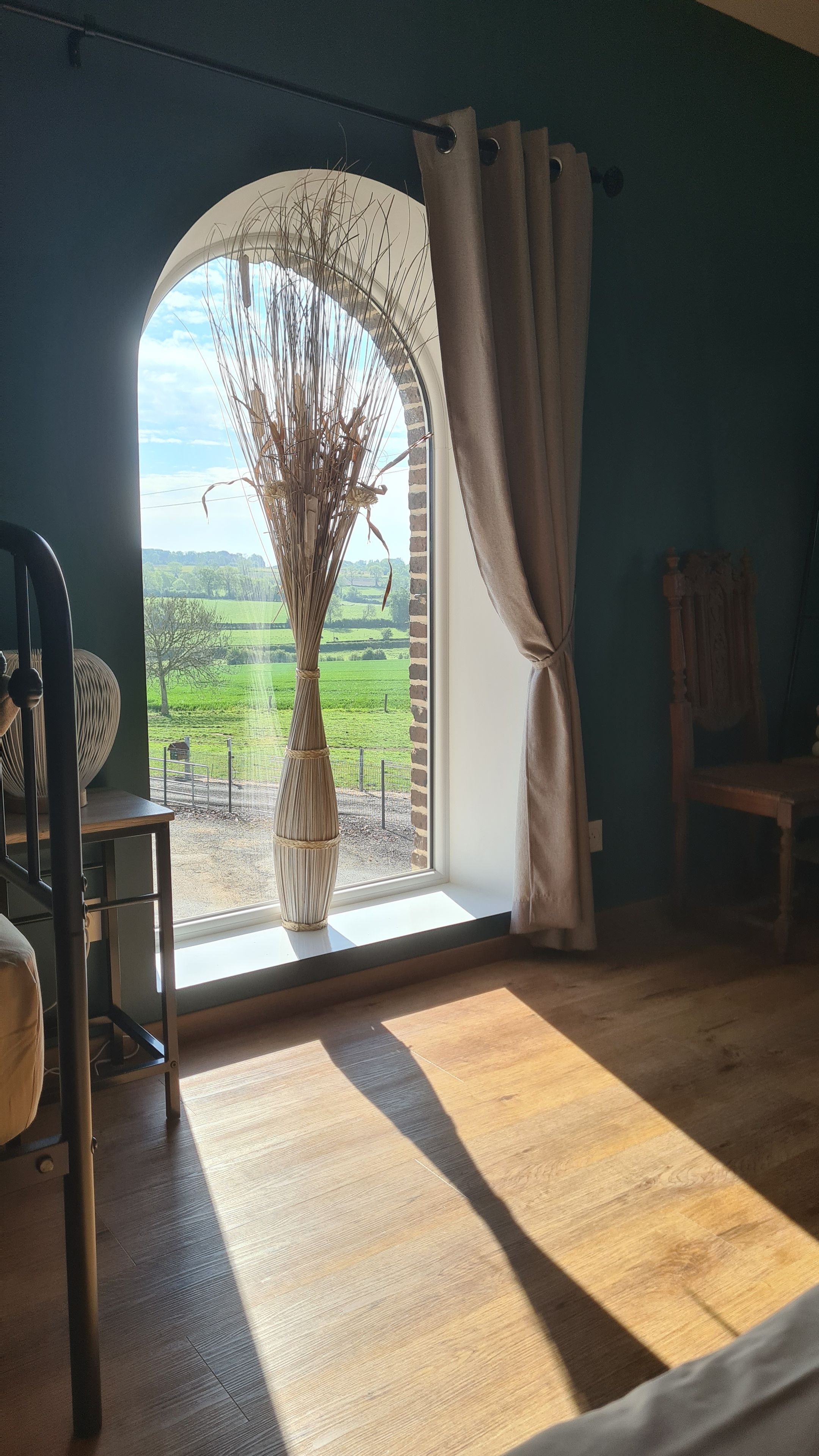 A room with a large window, a wooden floor, a chair, and a table.