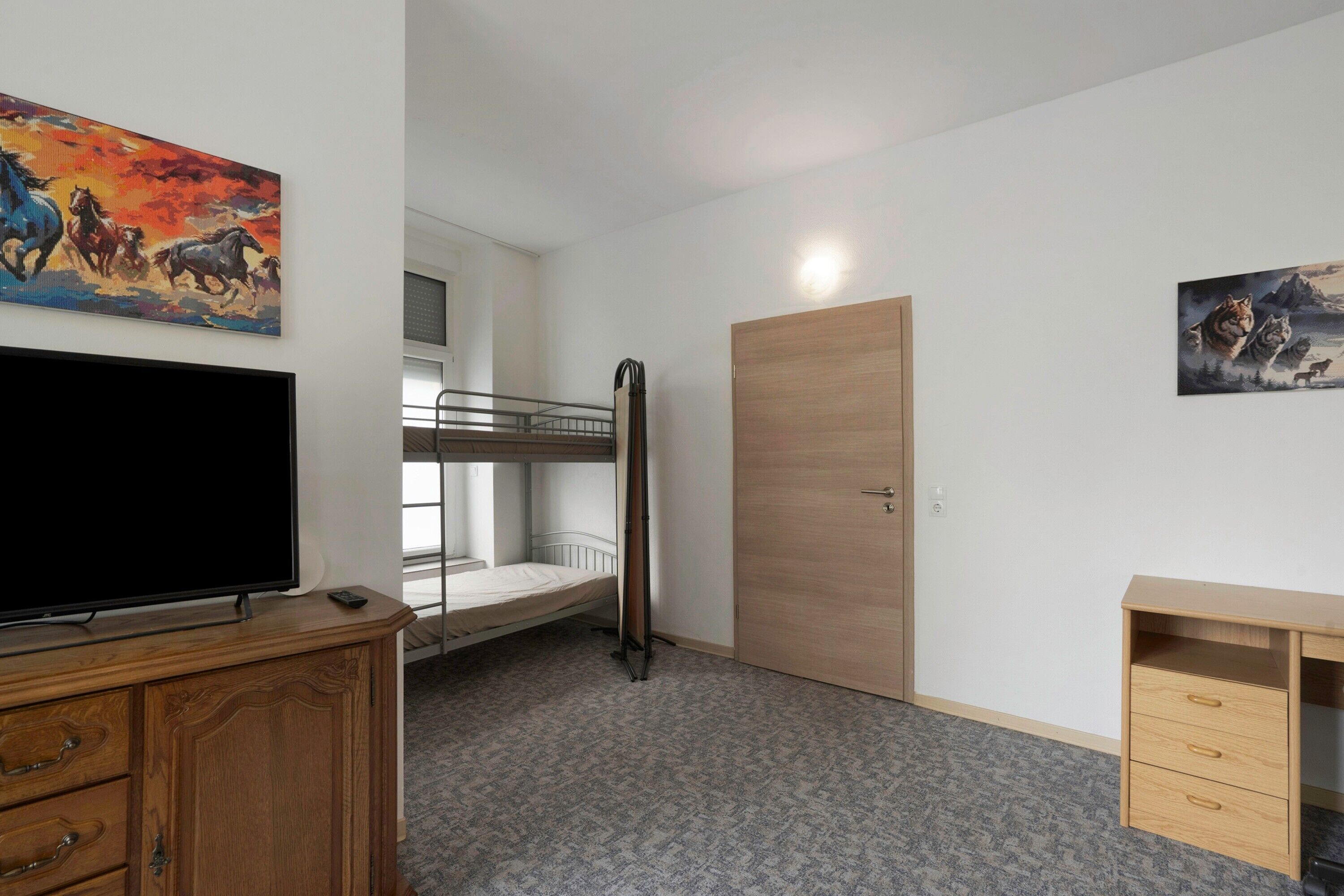 Ein Zimmer mit Etagenbetten, einem Fernseher, einem Schreibtisch und zwei Bildern.