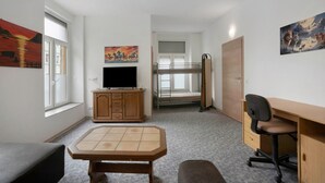 A room with a bunk bed, a desk, a television, and artwork on the walls.