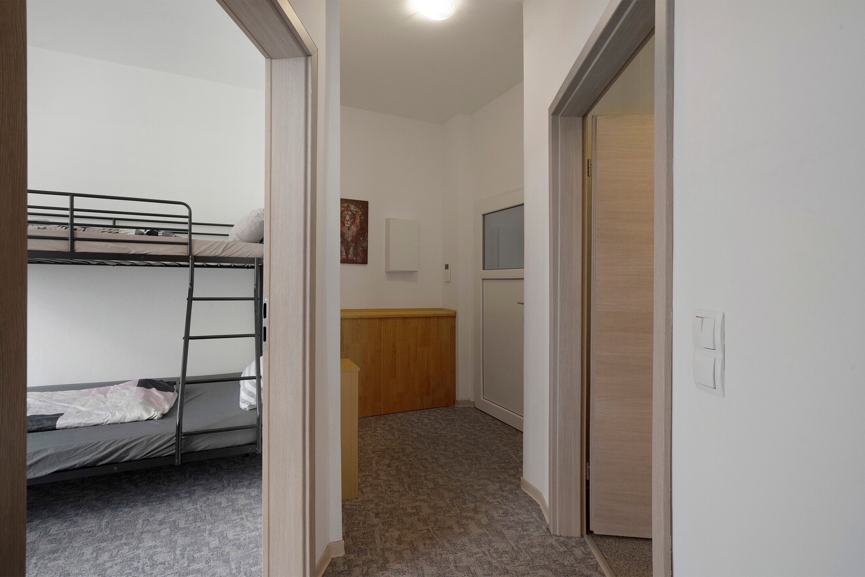 A room with bunk beds, a wooden cabinet, a small desk, and a door leading to another room.