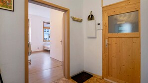 Un pasillo con una puerta de madera, un estante pequeño con una lámpara y un timbre.