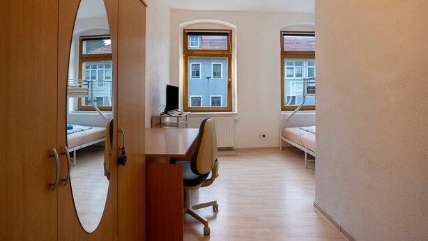 Una habitación con escritorio, dos camas, una silla y un espejo grande.