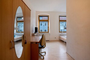 Una habitación con escritorio, dos camas, una silla y un espejo grande.