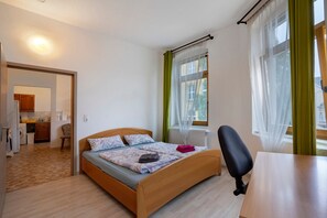 A bedroom with a bed, a chair, a table, a window with curtains, and a view of the outside.