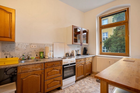 A kitchen with wooden cabinets, a stove, a sink, and a window with a view of trees.