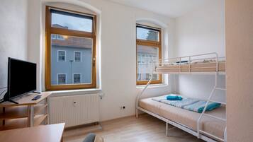 Ein Zimmer mit einem Etagenbett, einem Schreibtisch mit Computer, einem Fenster und einer Heizung.