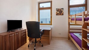 Een kamer met een bureau, een stoel, een televisie, stapelbedden en een raam.
