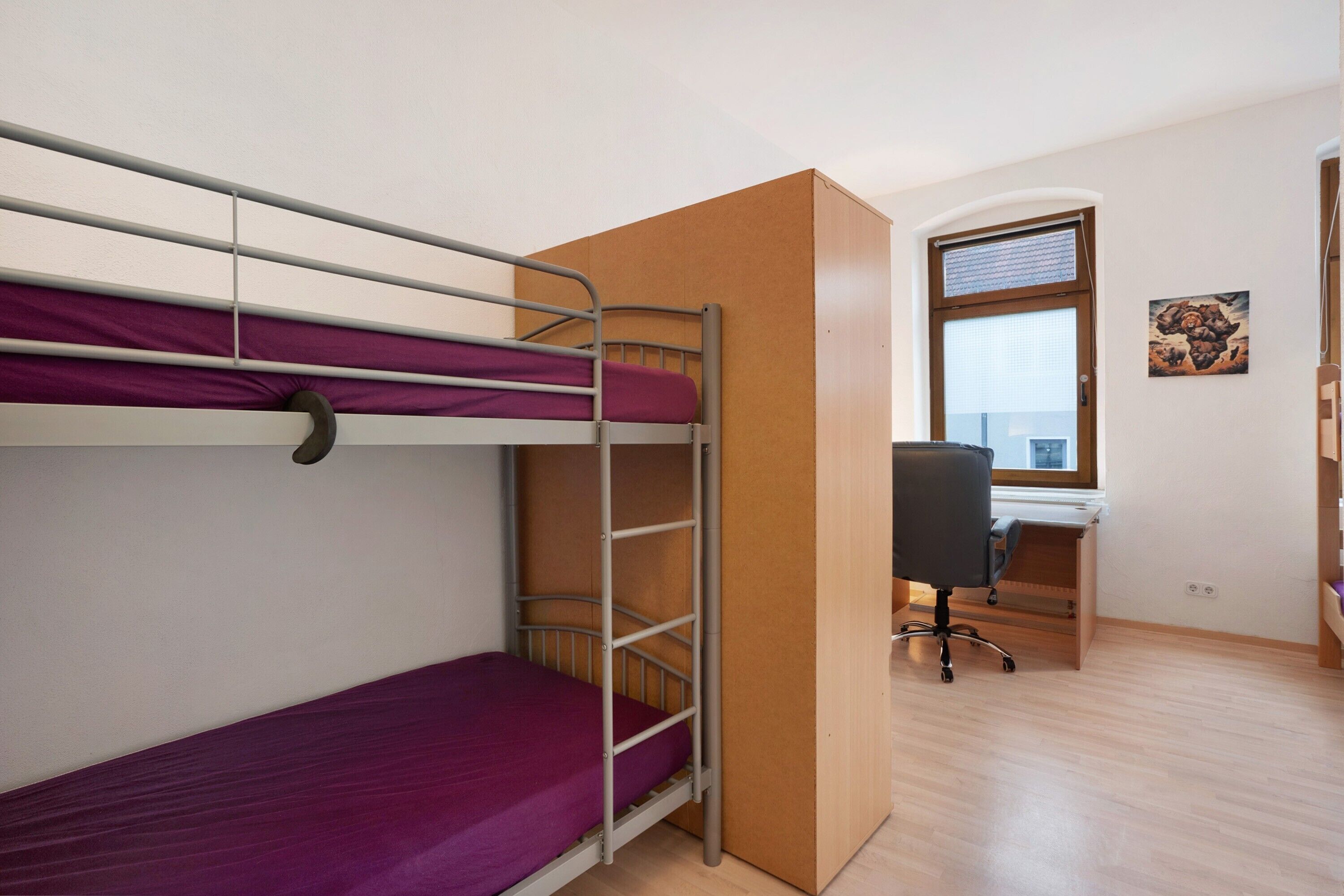 Una cama individual superpuesta con escritorio y silla, una ventana con persianas y un pequeño cuadro en la pared.