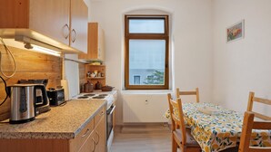 Een compacte keuken met houten kastjes, een raam en een eethoek met een tafel en stoelen.