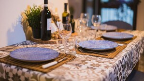 A dining table set with blue plates, wine bottles, and glasses, with a patterned tablecloth and a plant in the background. - Mare Tra i Tetti -  The sea among the rooftops (Monopoli)
