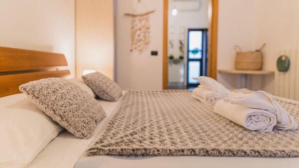A neatly made bed with a patterned blanket and rolled towels, a wooden headboard, and a wall-mounted decorative item. - Mare Tra i Tetti -  The sea among the rooftops (Monopoli)