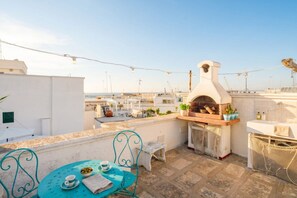 Una terraza en la azotea con horno de pizza, asientos exteriores y vistas al mar.