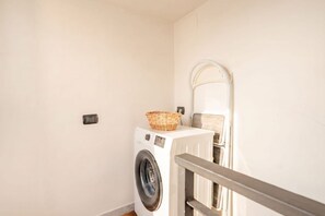 Une buanderie équipée d’un lave-linge, avec un panier posé sur le dessus et une rambarde en métal.