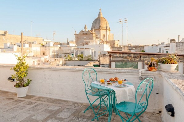 Una terraza en la azotea con una mesa preparada para dos, con vistas a un paisaje urbano de arquitectura histórica.