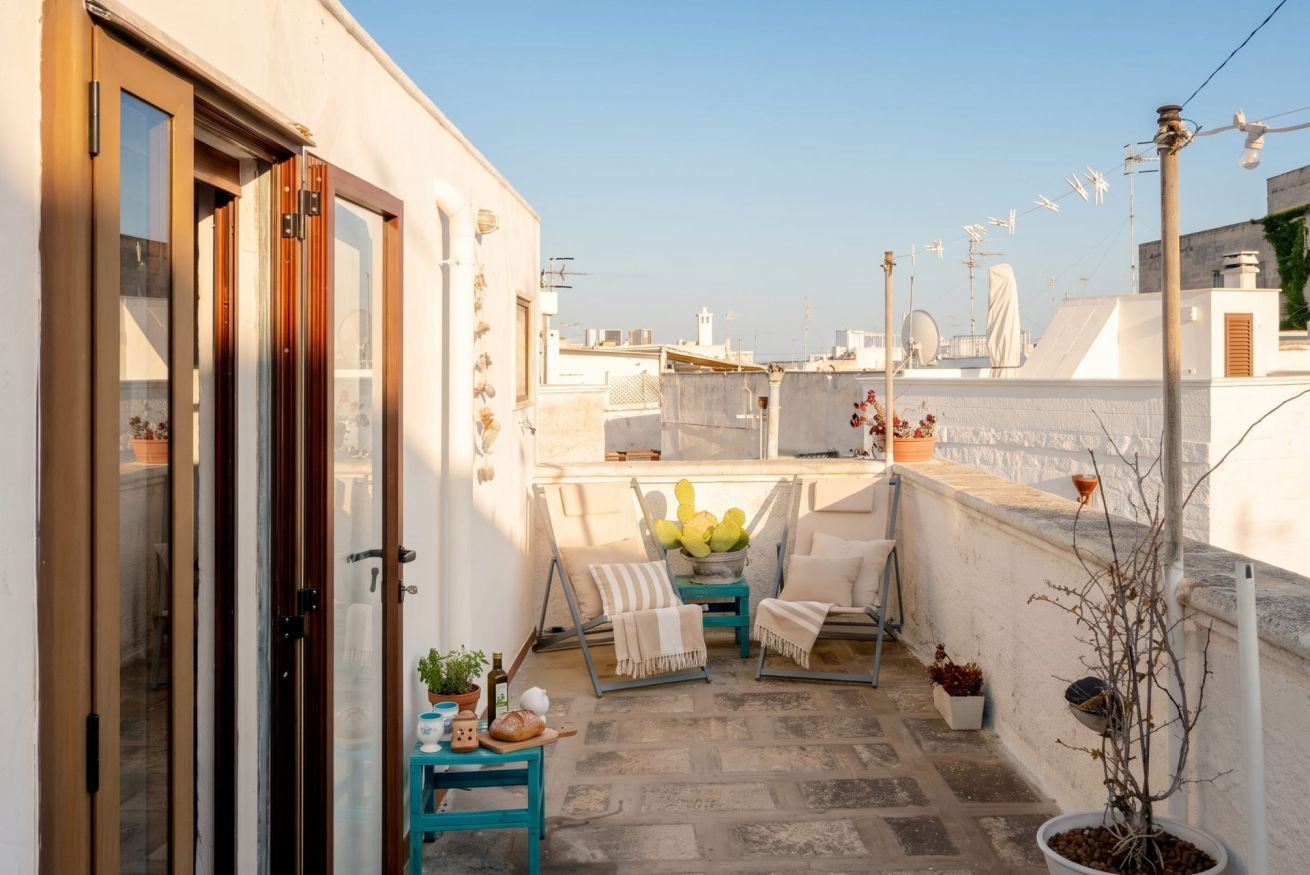 A rooftop terrace with a seating area, potted plants, and a view of the cityscape.