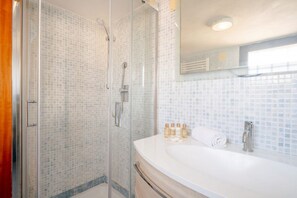 Un baño con ducha de vidrio, lavamanos blanco y espejo arriba.