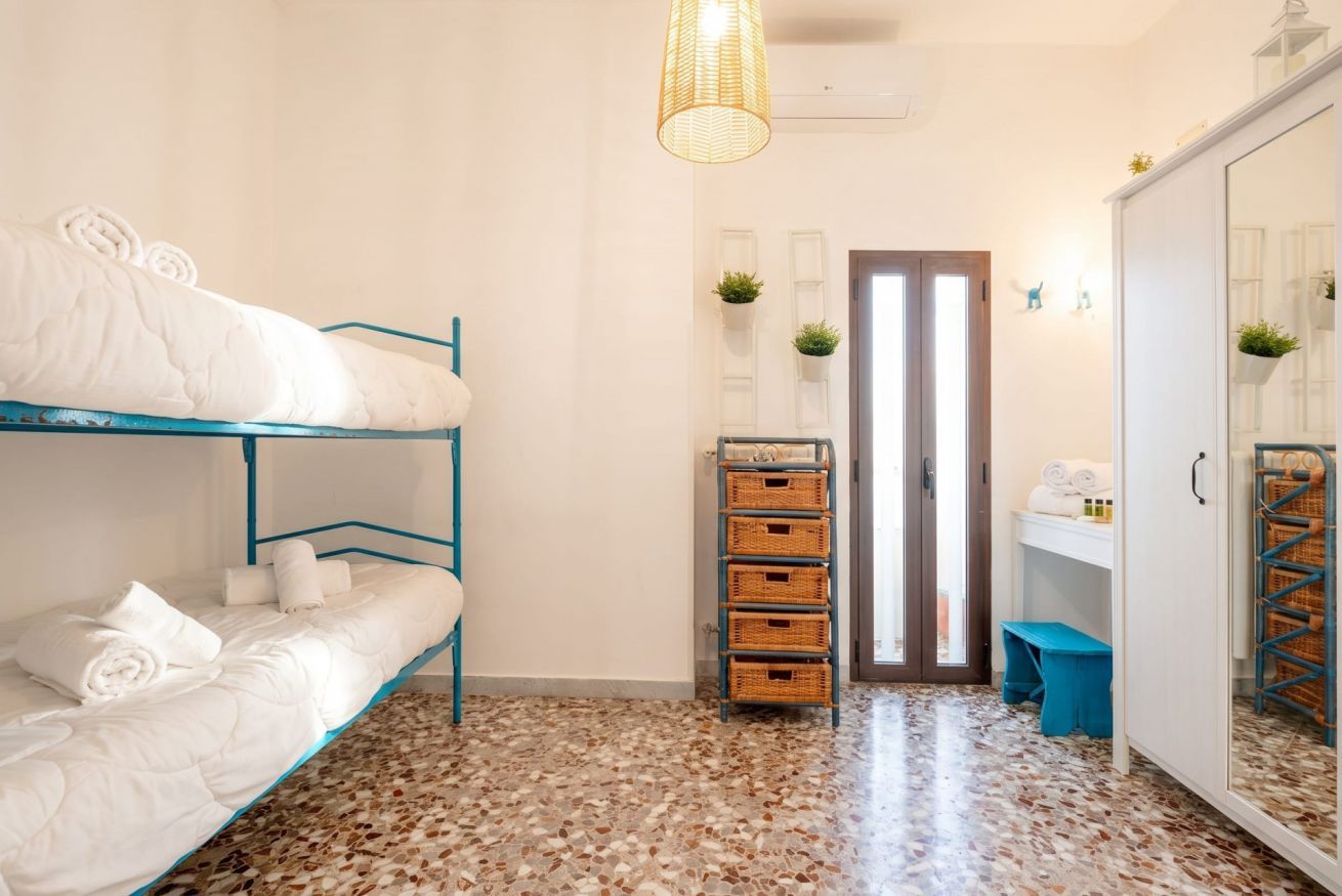 A room with bunk beds, a small bench, a mirror, and a door leading to another room.