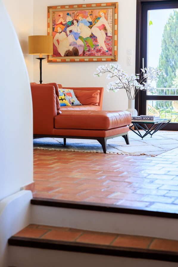 A living room with a sofa, a painting, a vase with flowers, and a view through a window.