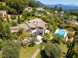 A Mediterranean-style villa with a swimming pool, surrounded by lush greenery and mountains in the background.