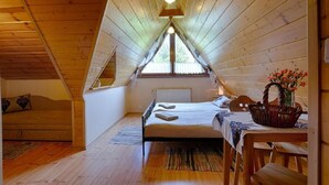 Een gezellig zolderkamer met schuine plafonds, een bed, een tafel met een mand en een raam dat natuurlijk licht binnenlaat.